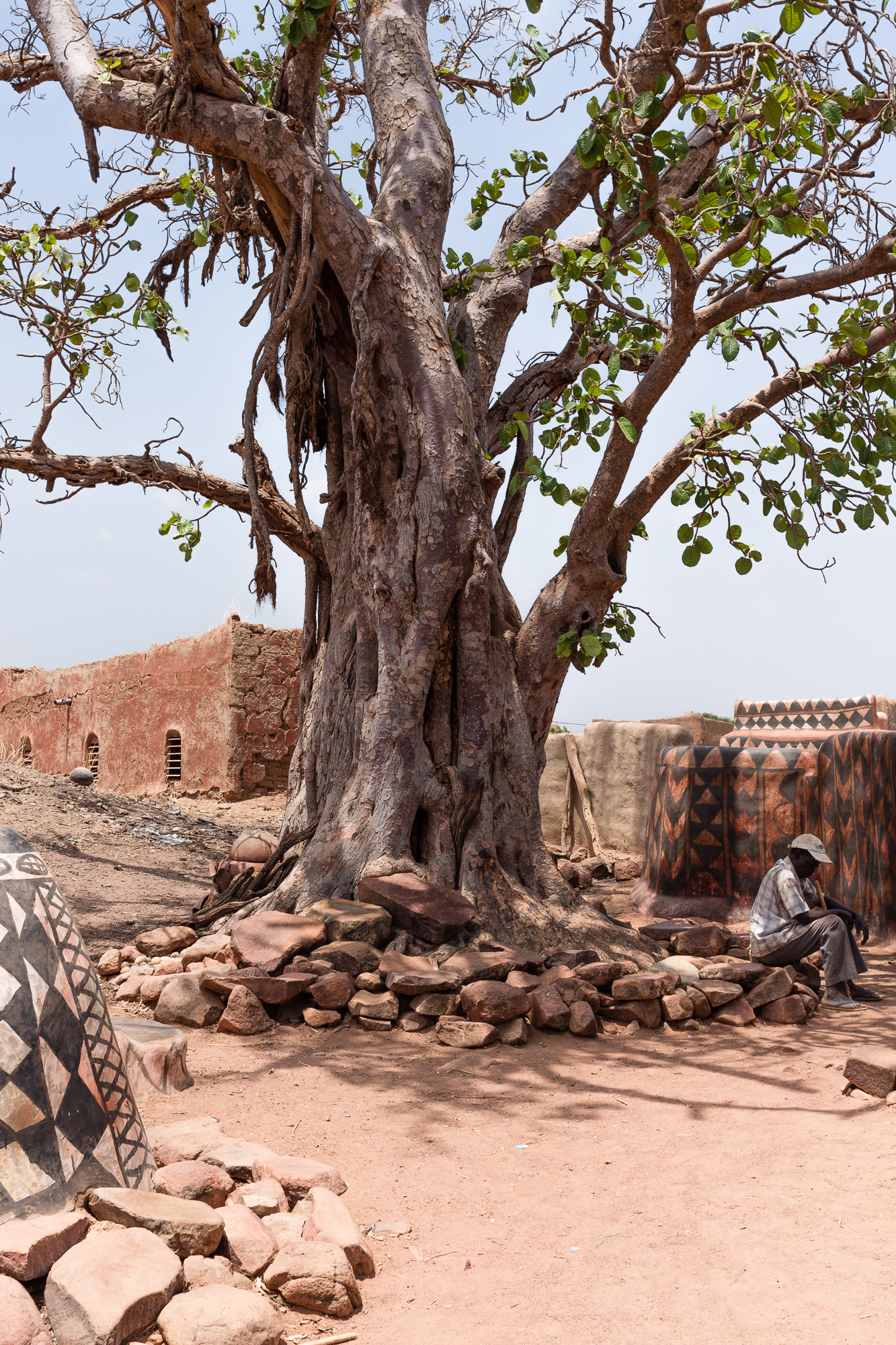Homme assis sur un tas de pierres disposées à l'ombre d'un arbre à l'entrée de la cour royale de Tiébélé, Burkina Faso