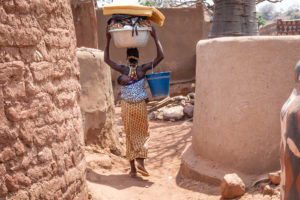 Femme avec enfant dans le dos et bassine remplie de linge sur la tête, dans les ruelles de Tiébélé, Burkina Faso