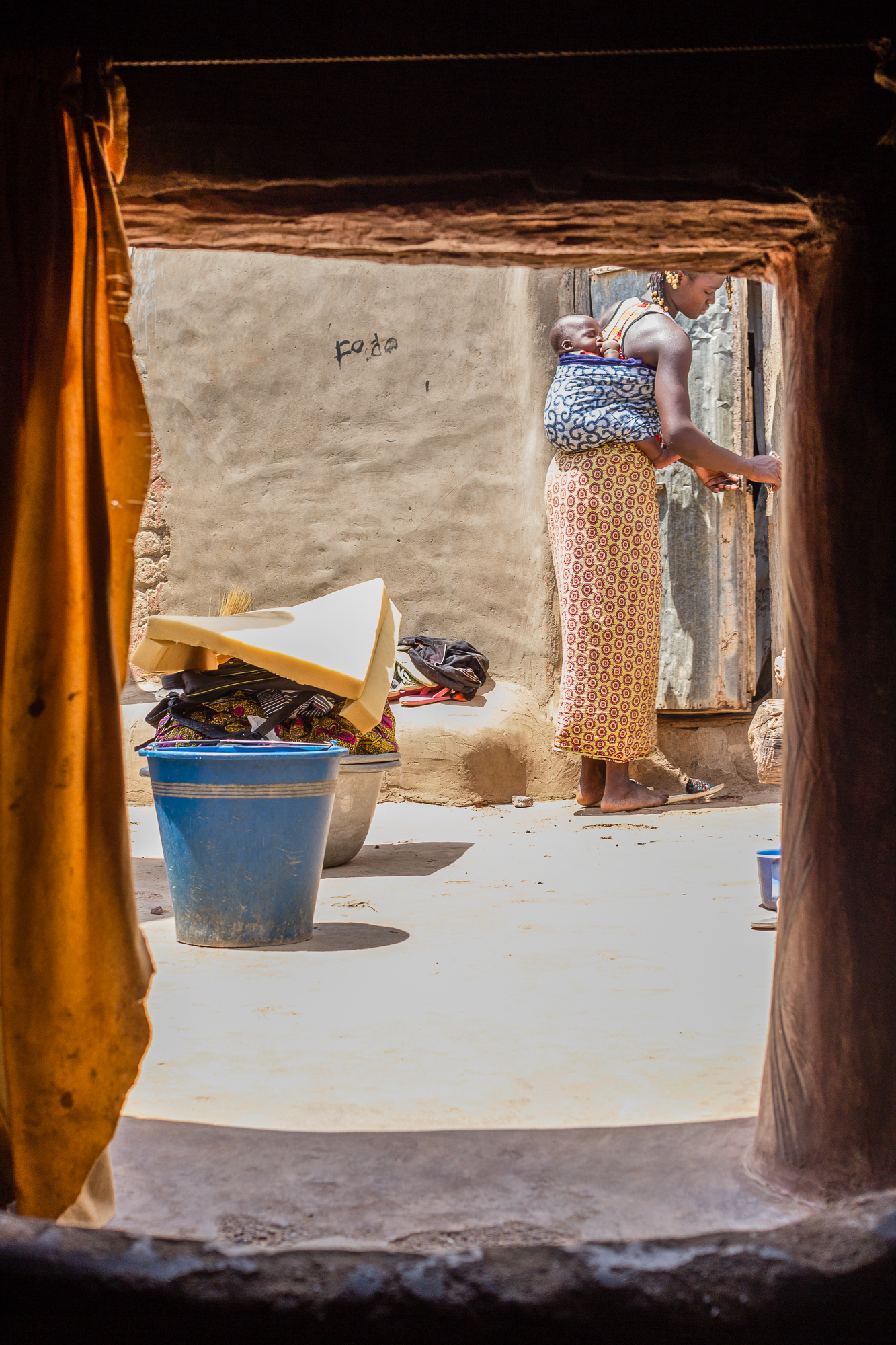 Femme avec enfant dans le dos fermant la porte de sa case, Tiébélé, Burkkina Faso