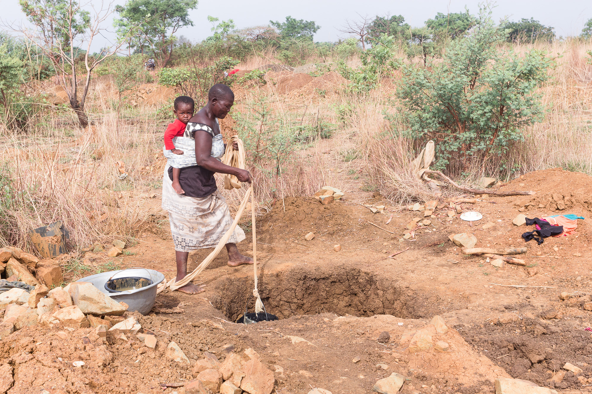 Chercheuse d'or avec enfant sur le dos descendant un seau dans un puits, pays Lobi, Burkina Faso