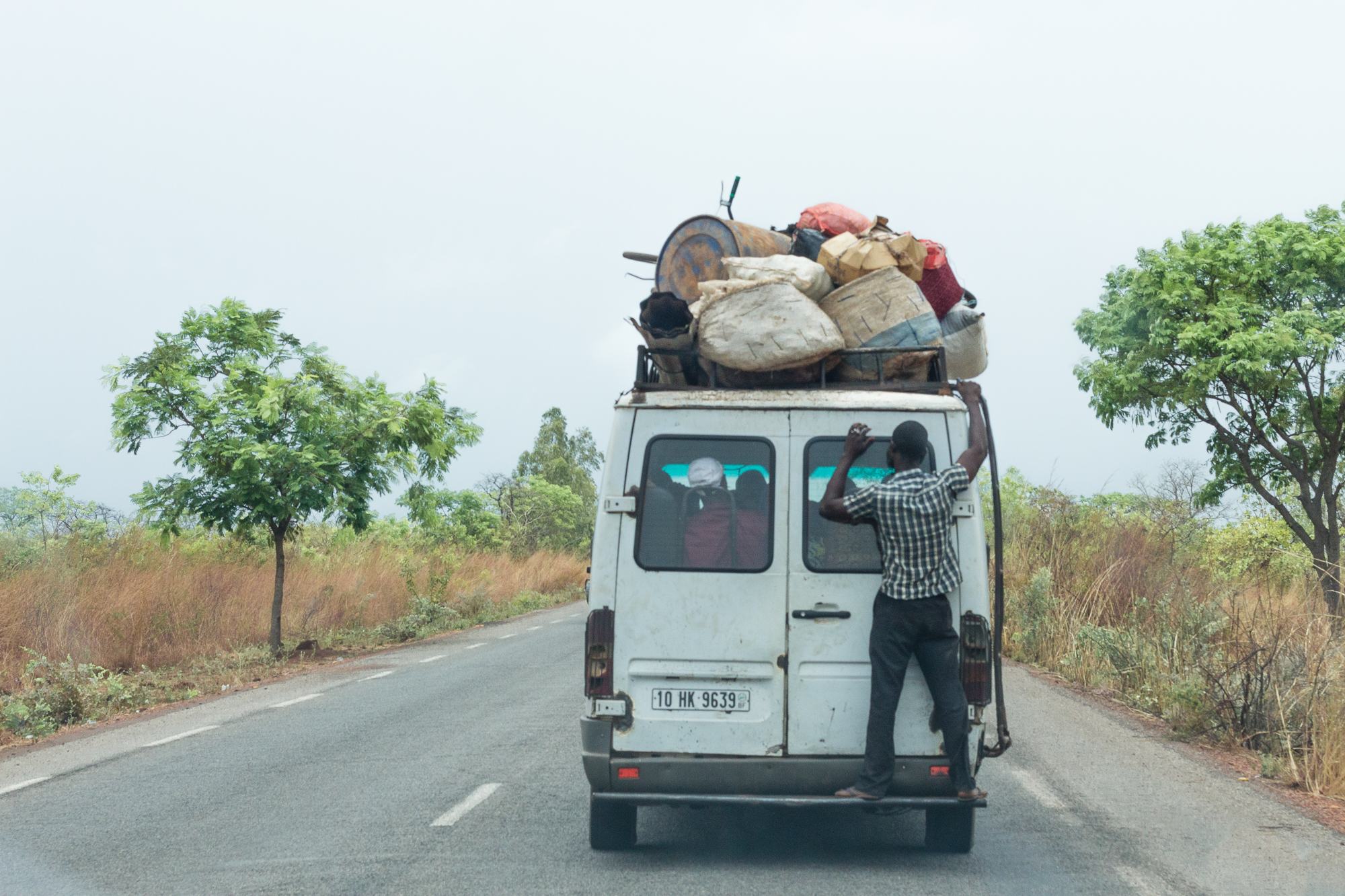 Un homme accroché à l'arrière d'un taxi-brousse très chargé, sur la route, Burkina Faso