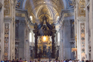 Sous la coupole de la Basilique Saint Pierre, nimbée de lumière, le baldaquin du Bernin et la foule de touristes, Vatican