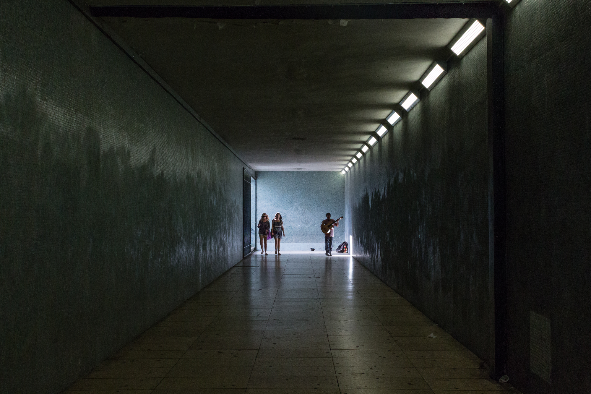 Musicien et passantes au fond d'un tunnel, rai de lumière, Lisbonne, Portugal