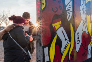 Touristes utilisant un téléphone devant une fresque du mur de Berlin et rayon de soleil
